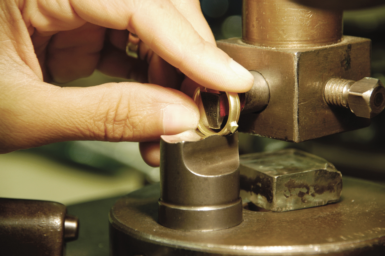 A gold ring is being held between a persons' thumb and forefinger and shaped using bench tools.