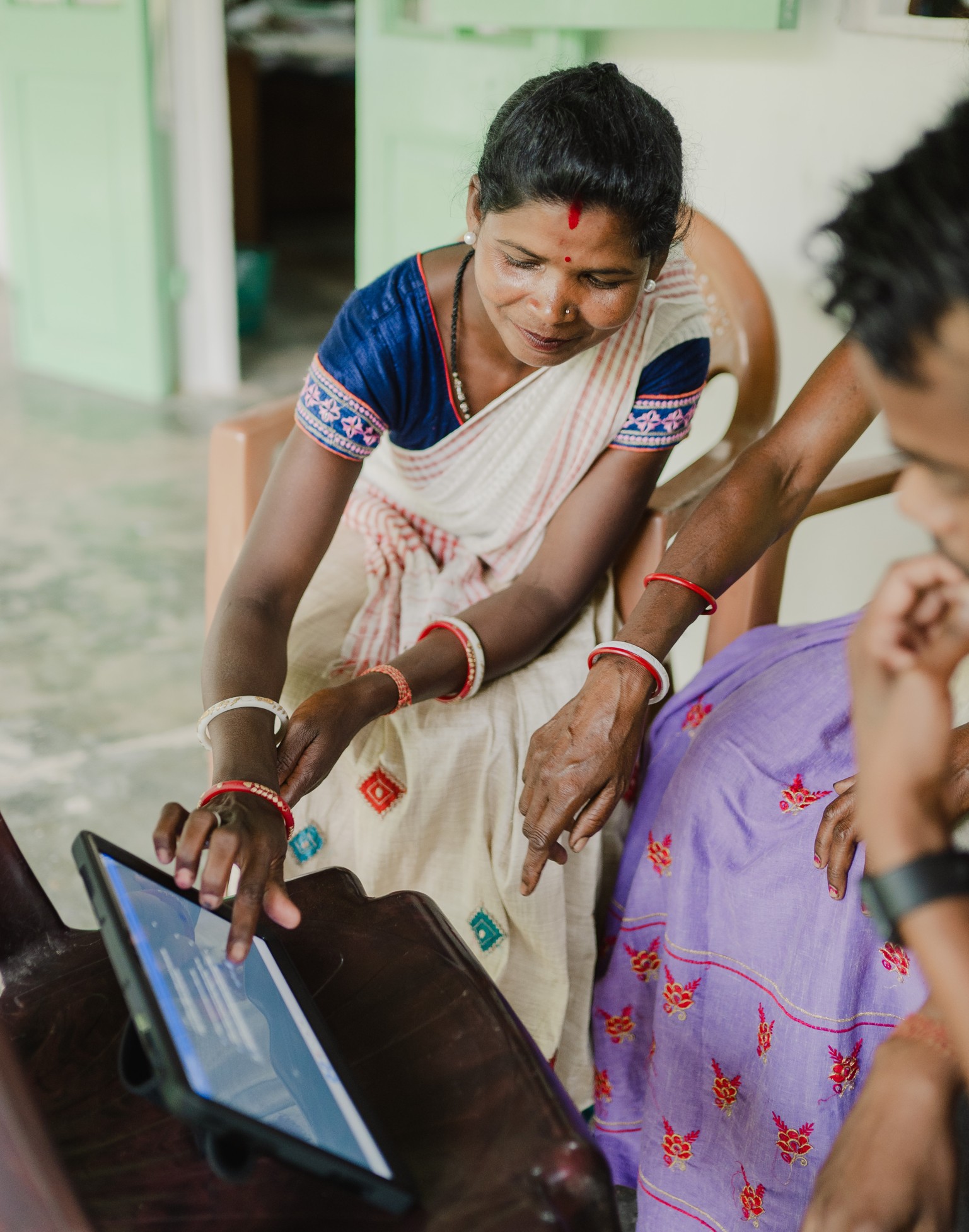Two Indian women sit, interacting with a tablet computer.