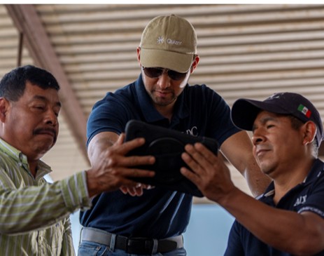 three Mexican men in baseball caps looking at a tablet computer. 