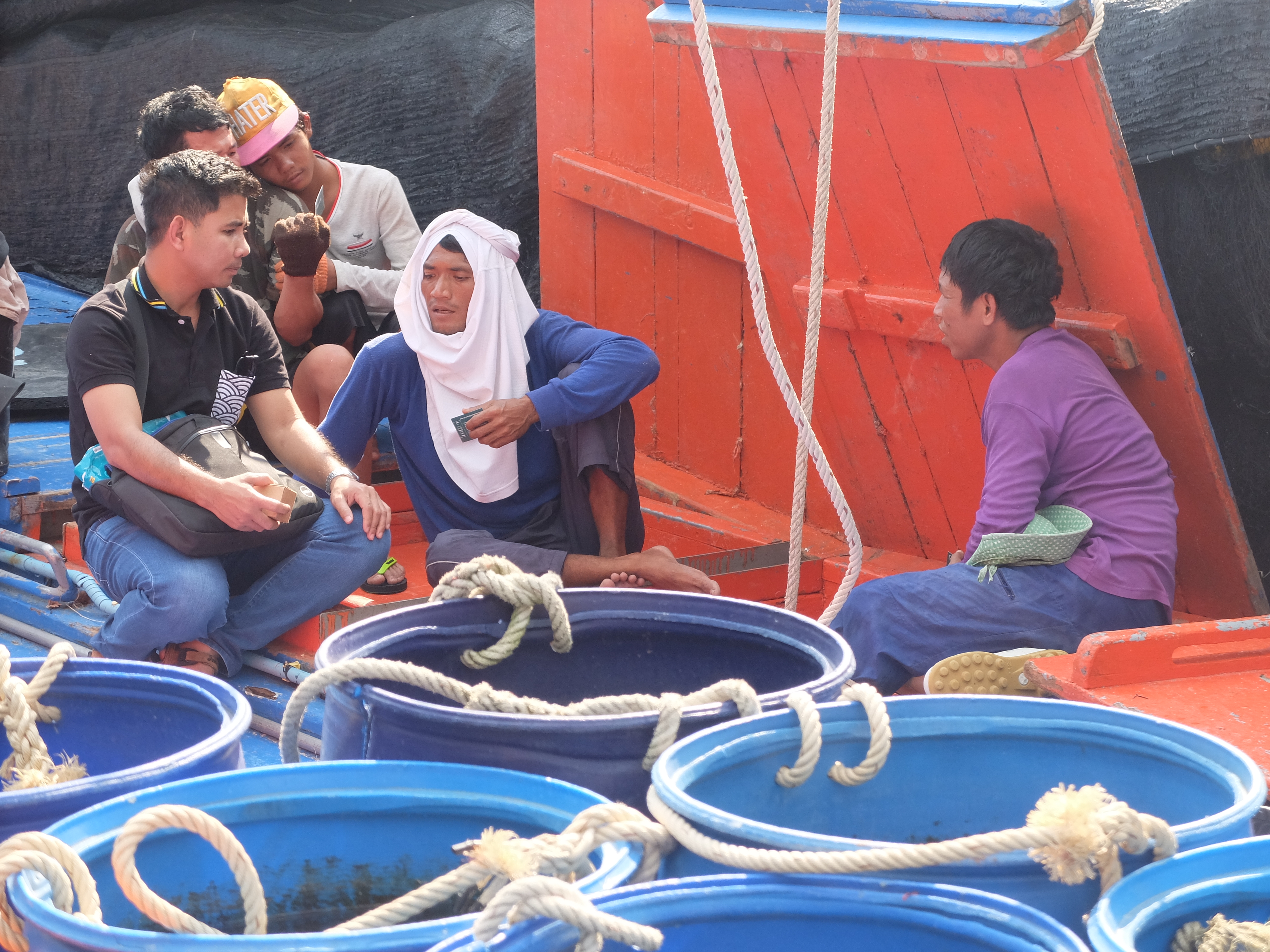 Issara fishermen workers on a boat in the shade surrounded by buckets
