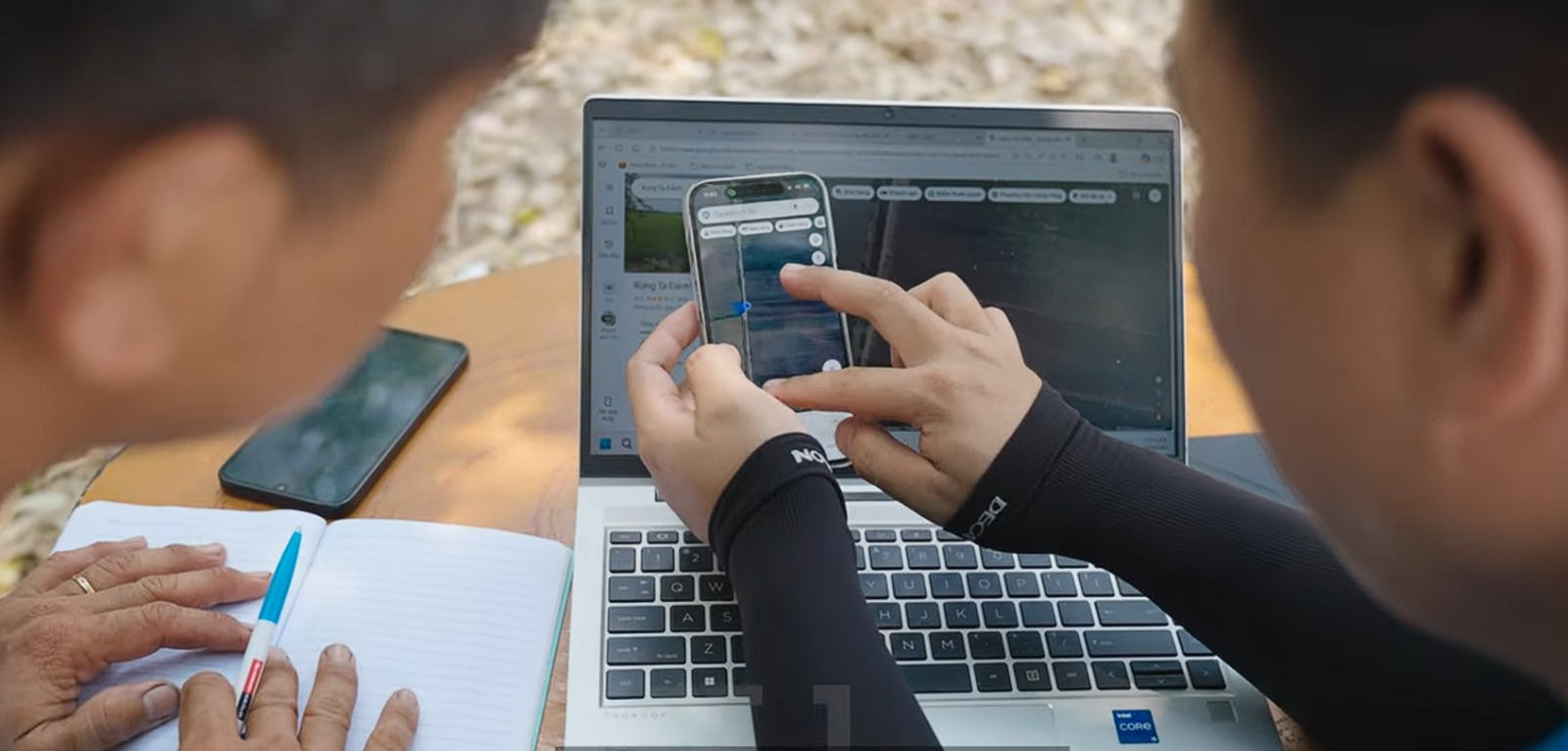 Two people look at data on a mobile phone in front of a laptop