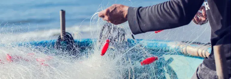 Fishing nets on a boat on the sea and a person pulling it © Adobe Stock