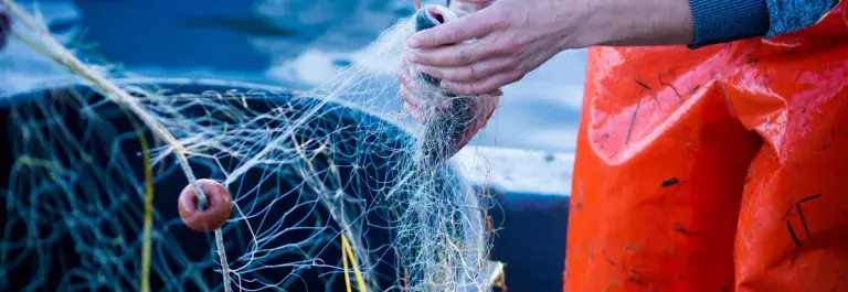 A fisher stands by a net wearing red waders © Adobe Stock