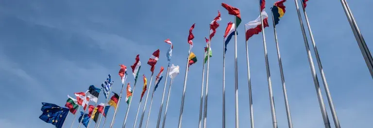 Looking up at flags of different countries against a mostly blue sky © Adobe Stock
