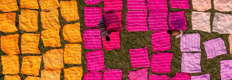 Aerial shot of orange, pink and purple textile clothes being laid out by two people © Adobe Stock