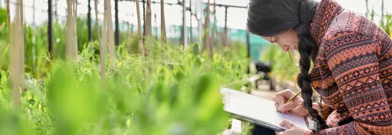 Woman collecting data by taking notes next to various plants © Adobe Stock
