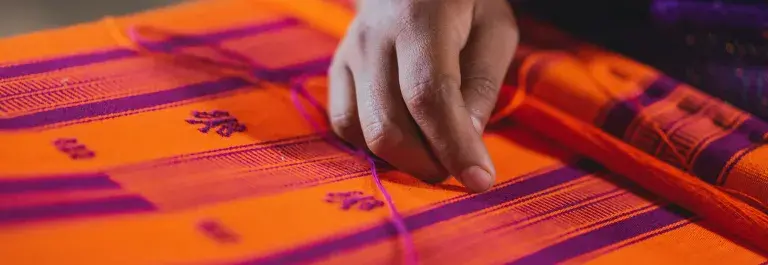 Person weaving orange and purple patterned fabric © Pexels