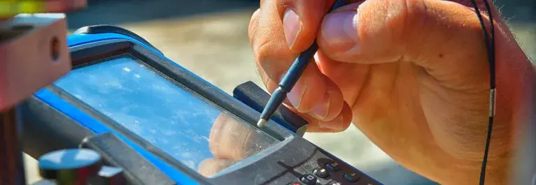 A hand using a stylus tool to interact with a black and blue electronic device with an LCD and keypad © Adobe Stock