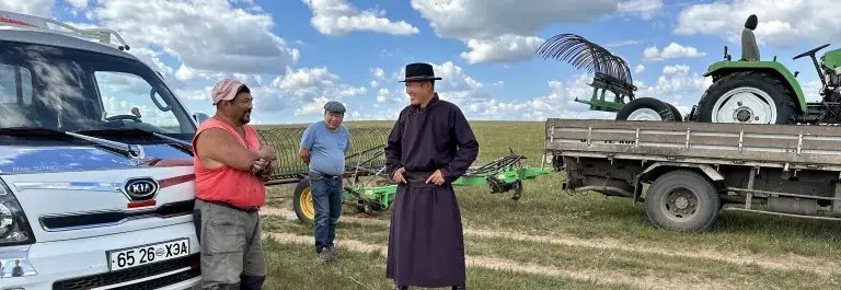 Mongolia pastoralists standing in front of agricultural equipment on a green plain. © Sustainable Fibre Alliance