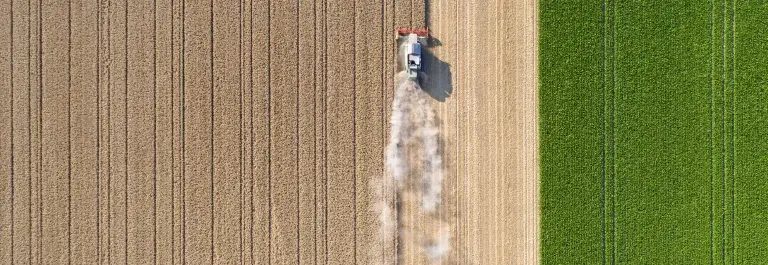 Birds eye view of farming equipment collecting crops from brown and green fields