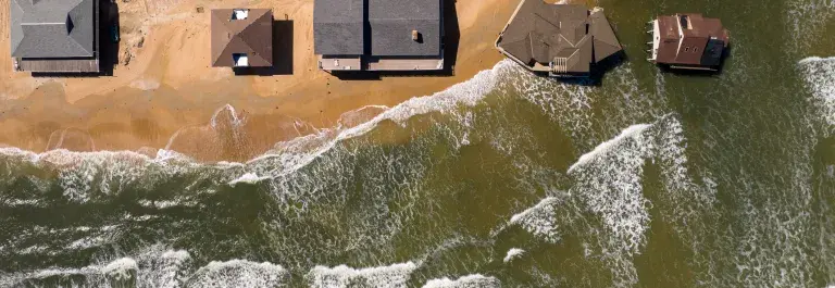 Aerial view of houses on a coastline with two on stilts in the water