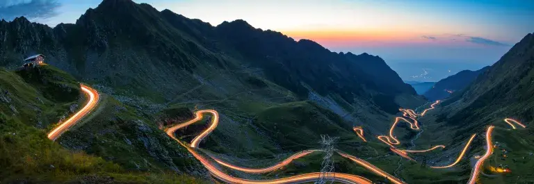 Mountain landscape with brightly lit winding road at dusk © Adobe Stock