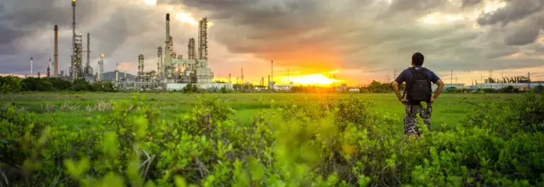 Man in a field next to a factory looking out at the sunset © Adobe Stock