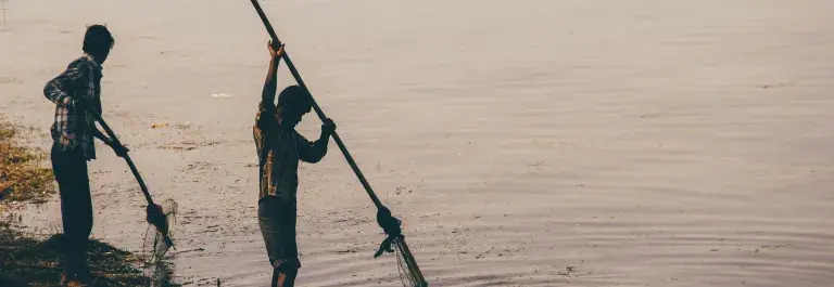 Two people fishing by the side of a river with nets © Unsplash