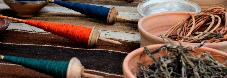 Spools of green, orange, blue, and yellow thread sit opposite corresponding bowls of dried plants used in the dye-making process