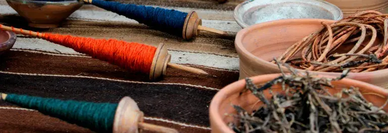 Spools of green, orange, blue, and yellow thread sit opposite corresponding bowls of dried plants used in the dye-making process.