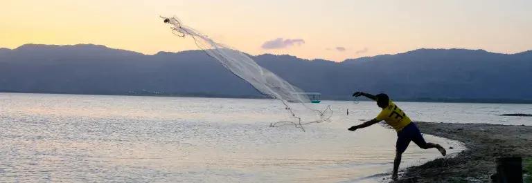 Fisherman throwing net into the sea from the beach in the sunset