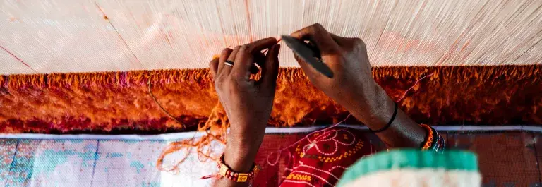 Textile worker weaving threads surrounded by red fabric © GoodWeave