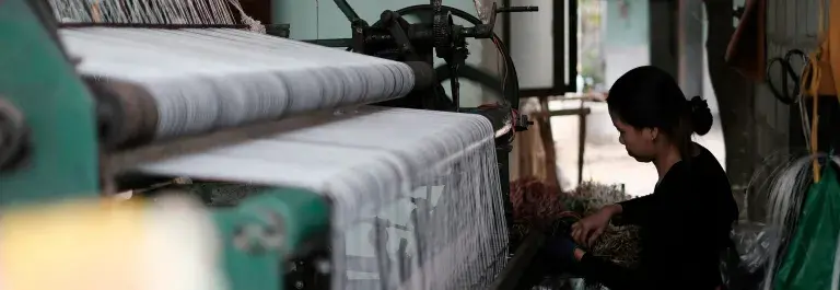 Woman textile worker sitting by weaving equipment with white yarn © Unsplash