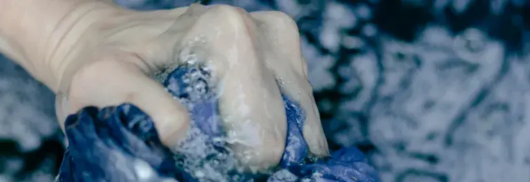 A pair of hands wring blue fabric over a swirling vat of dye © Pexels
