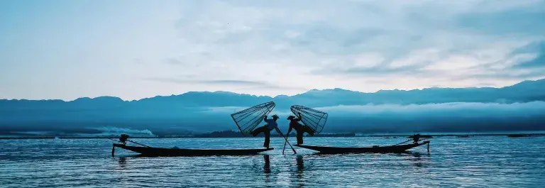 Fishers balancing on the end of their boats holding hands and carrying fishing cages © Pexels