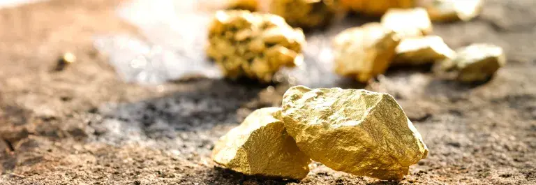 Nuggets of brightly shining gold ore on a brown rock surface © Adobe Stock