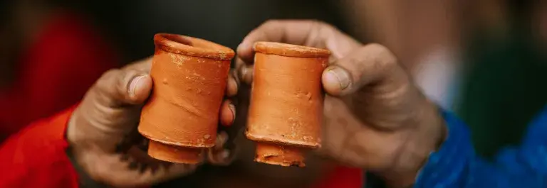 Two people holding two clay cups in their hands and holding them together to cheers