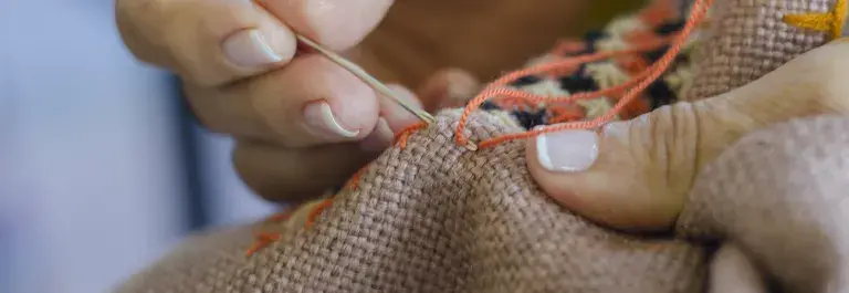 Person sewing fabric with orange thread and needle © Adobe Stock