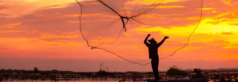 Fisherman net being cast with an orange and yellow sunset sky © Adobe Stock