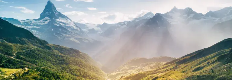 Swiss landscape of mountains and green trees with the sun shining down © Adobe Stock