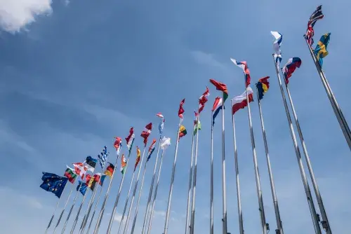 Looking up at flags of different countries against a mostly blue sky