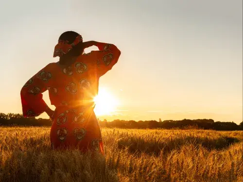 Woman looking out across wheat field in the sunset © Adobe Stock
