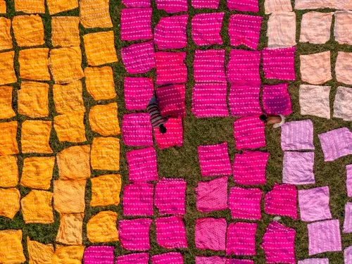 Aerial shot of orange, pink and purple textile clothes being laid out by two people © Adobe Stock