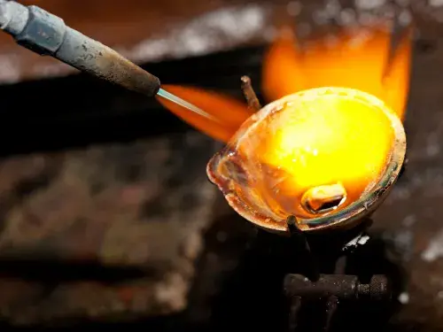 A blowtorch is heating a metal crucible, creating a jet of yellow-orange flame © Adobe Stock