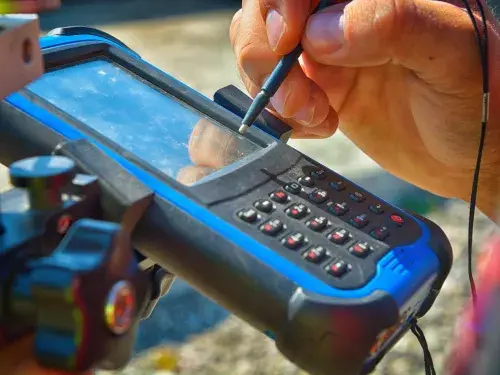 A hand using a stylus tool to interact with a black and blue electronic device with an LCD and keypad &copy; Adobe Stock