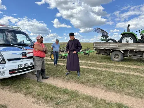 Mongolia pastoralists standing in front of agricultural equipment on a green plain © Sustainable Fibre Alliance