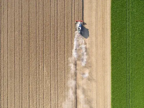Birds eye view of farming equipment collecting crops from brown and green fields