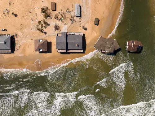 Aerial view of houses on a coastline with two on stilts in the water