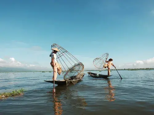 Two people wearing traditional rice hats on small fishing boats with large cages and oars against the blue sky © Unsplash