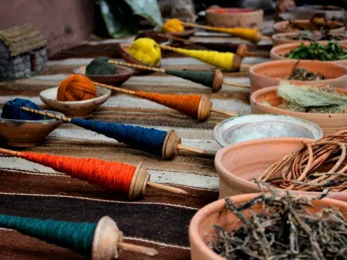 Spools of green, orange, blue, and yellow thread sit opposite corresponding bowls of dried plants used in the dye-making process