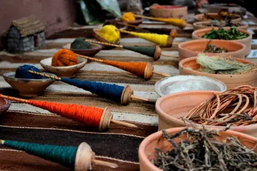 Spools of green, orange, blue, and yellow thread sit opposite corresponding bowls of dried plants used in the dye-making process.