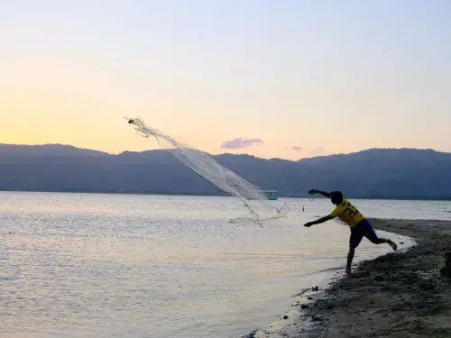 Fisherman throwing net into the sea from the beach in the sunset