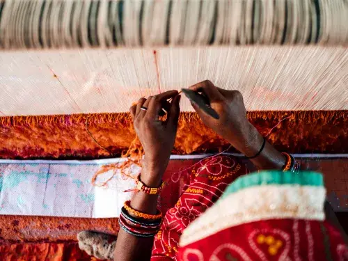 Textile worker weaving threads surrounded by red fabric © GoodWeave