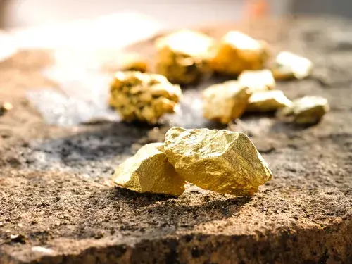 Nuggets of brightly shining gold ore on a brown rock surface © Adobe Stock
