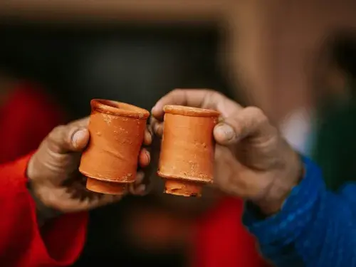Two people holding two clay cups in their hands and holding them together to cheers