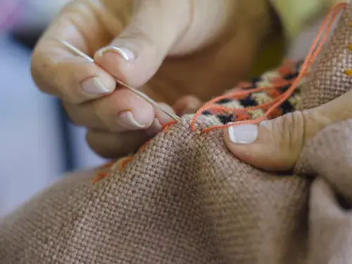 Person sewing fabric with orange thread and needle © Adobe Stock