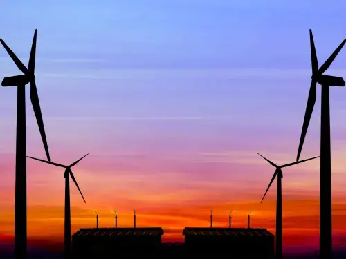 The silhouettes of four wind turbines stand against a blue sky at dusk with an orange sunset on the horizon