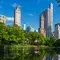 New York City skyscrapers from Central Park with green trees and a bright blue sky
