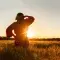 Woman looking out across wheat field in the sunset © Adobe Stock