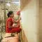Woman weaving textiles in a red outfit and brick background